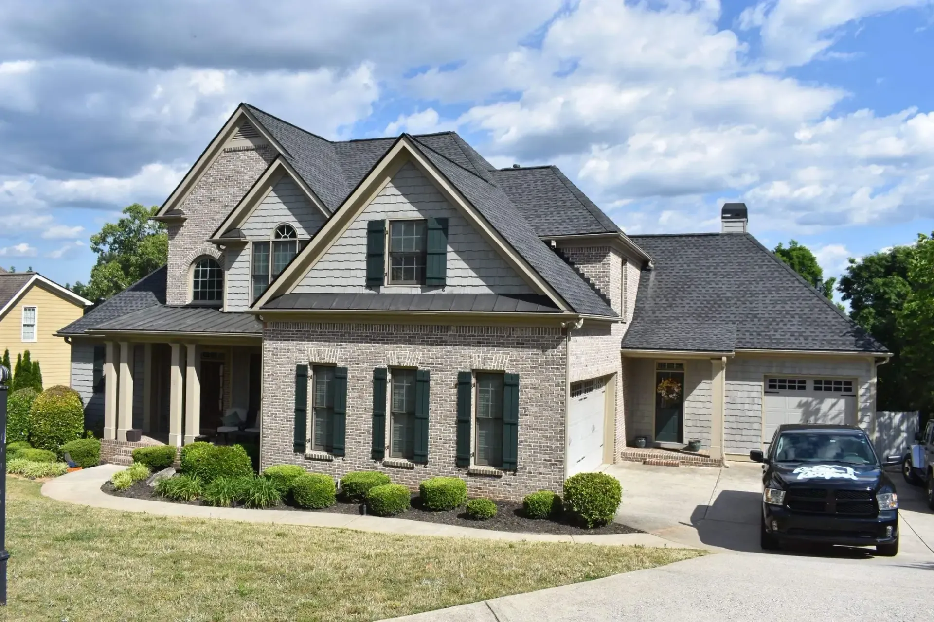 Two-story brick house with gray roof, green shutters, and a black truck in the driveway.