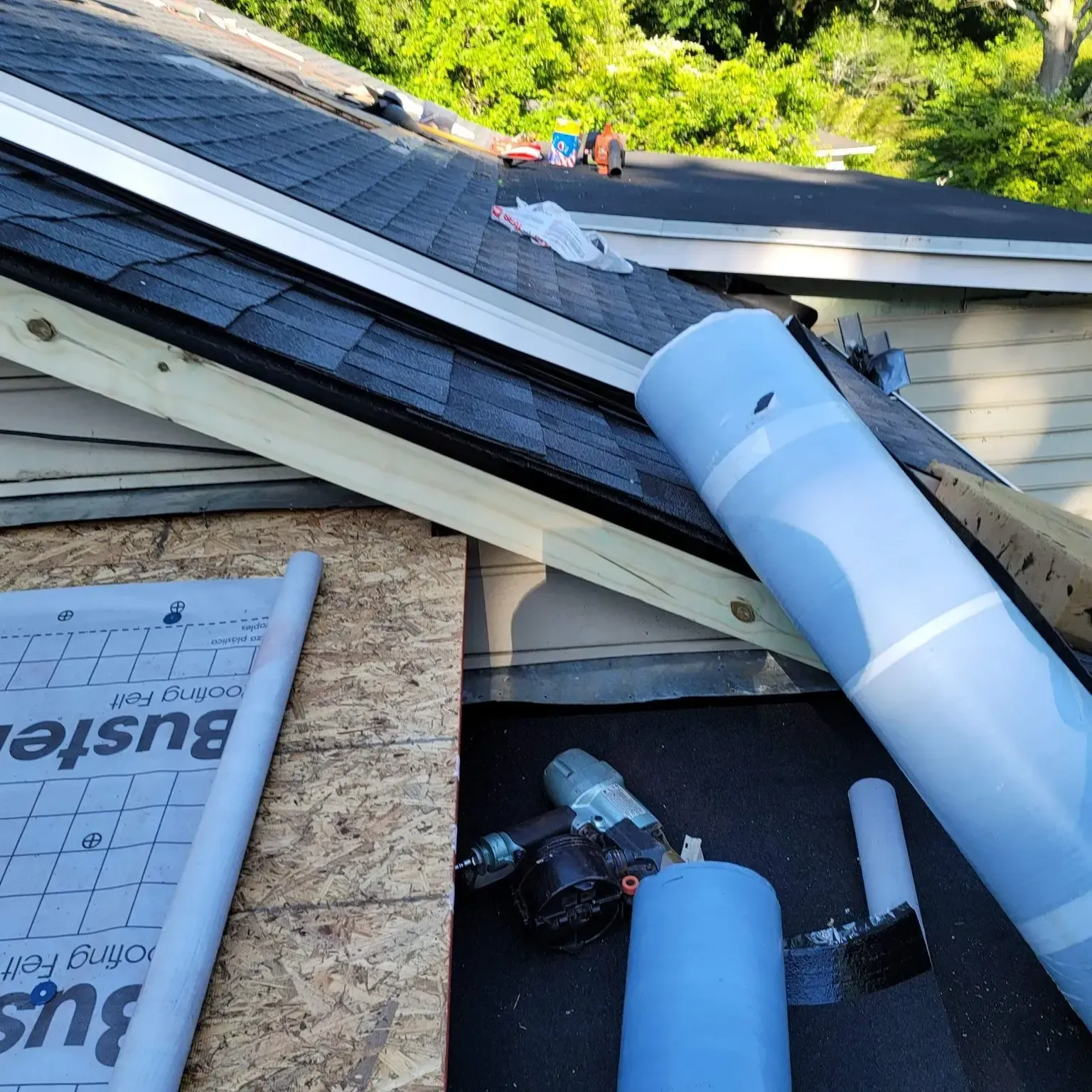 Roof being repaired; roll of blue underlayment and tools on a shingled roof, lumber.