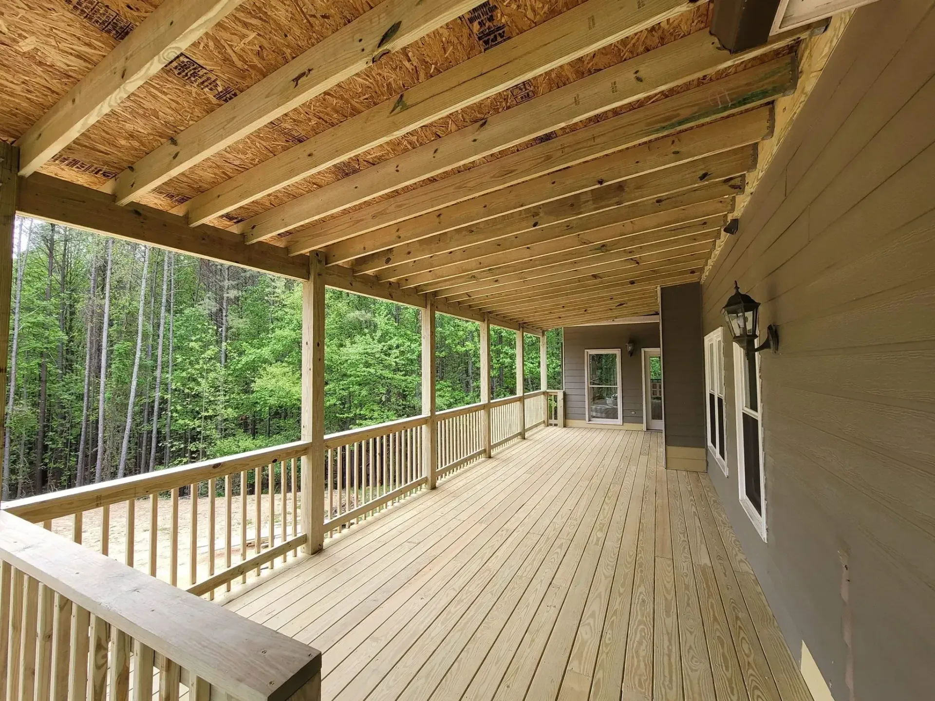 Wooden porch with railing and exposed beams overlooking a forest.