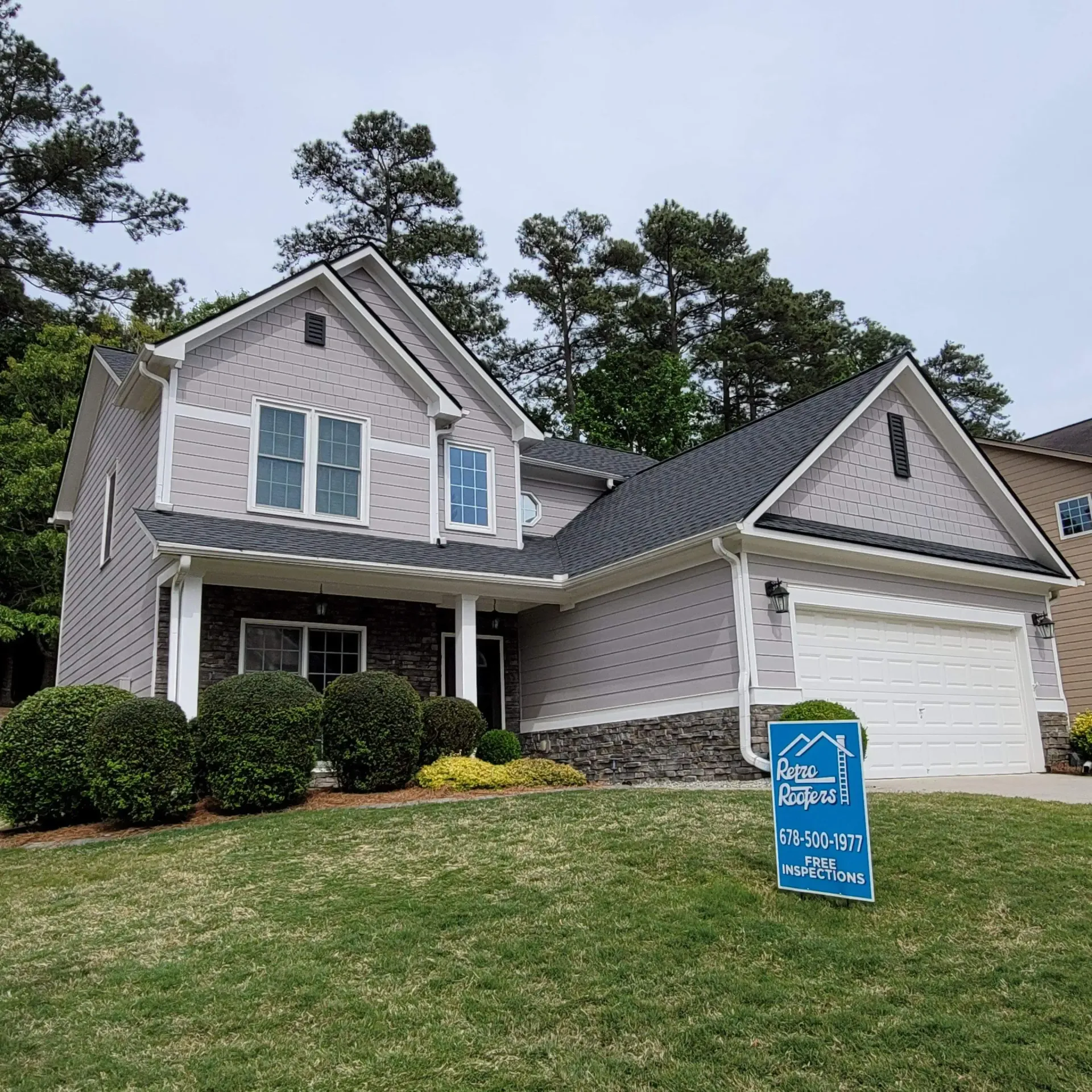 Two-story house with gray siding, dark roof, and white garage door; sign on front lawn.