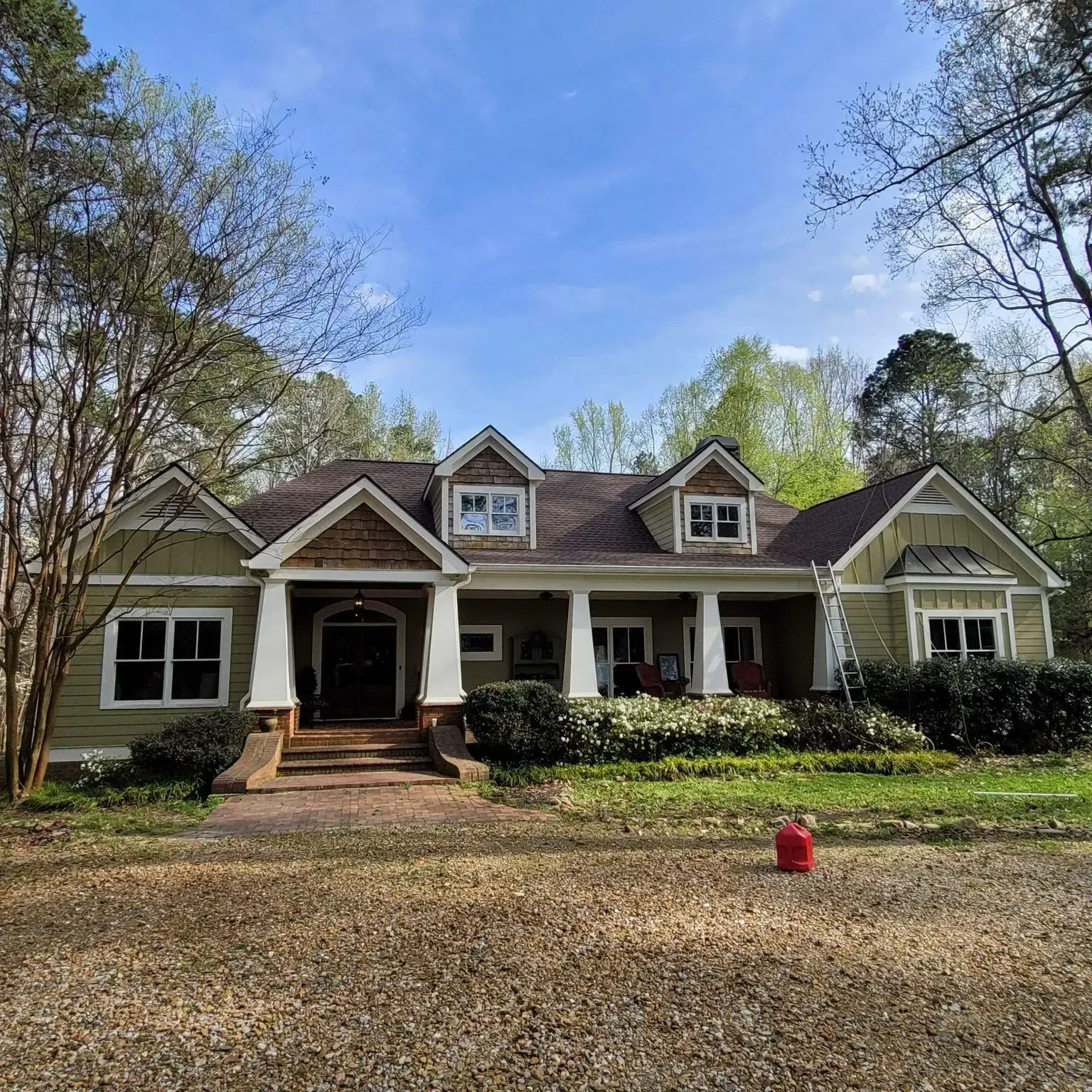 Green house with white columns, brown roof, and landscaping under a blue sky.