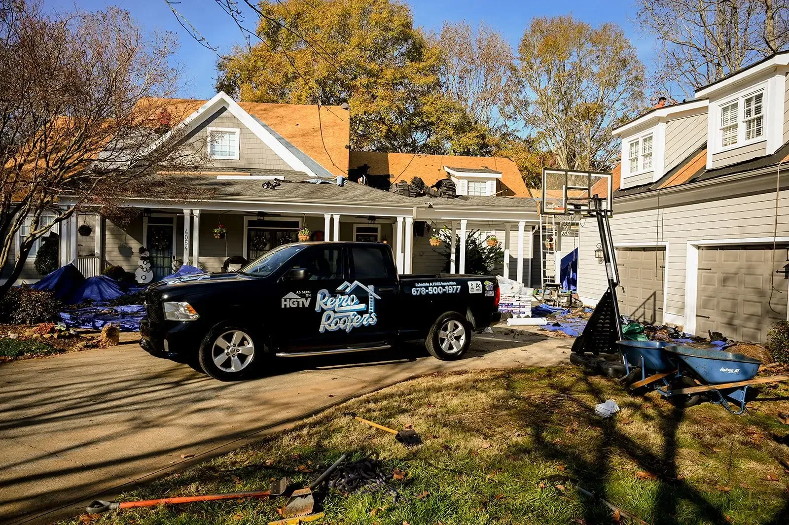 Black truck parked in front of a house with roofing in progress; autumn trees and clear sky.