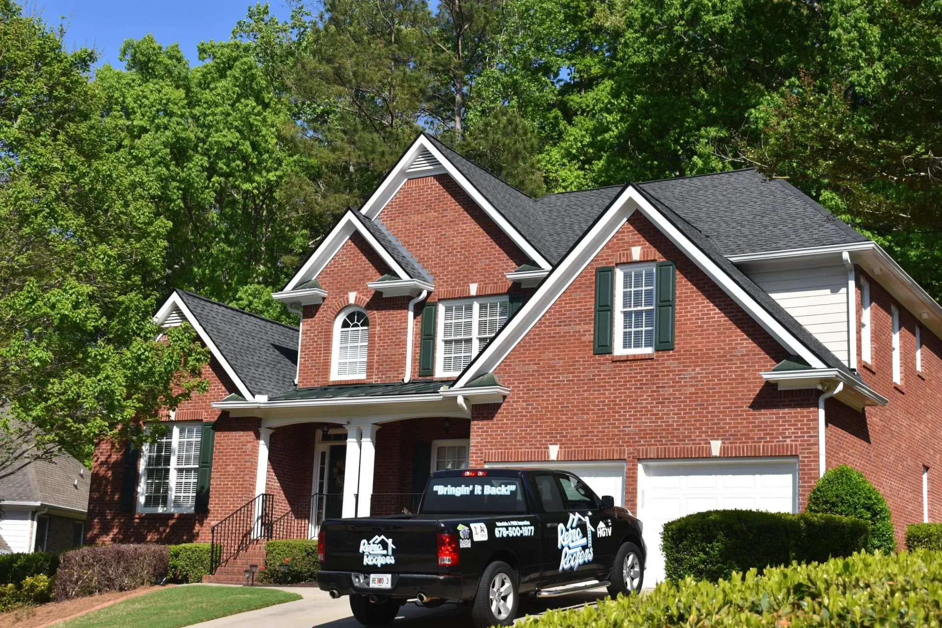 Red brick house with black roof, green shutters, and a black truck parked in the driveway.