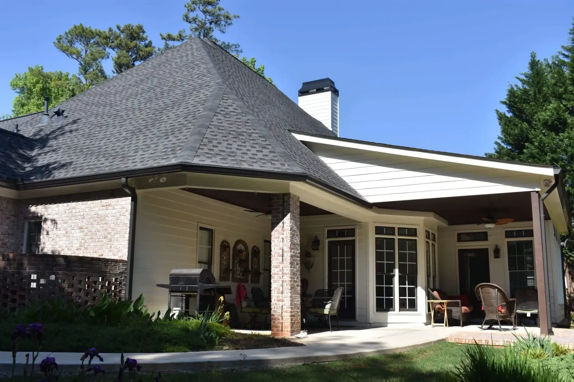 White house with a dark roof and covered porch, barbecue, and outdoor seating.