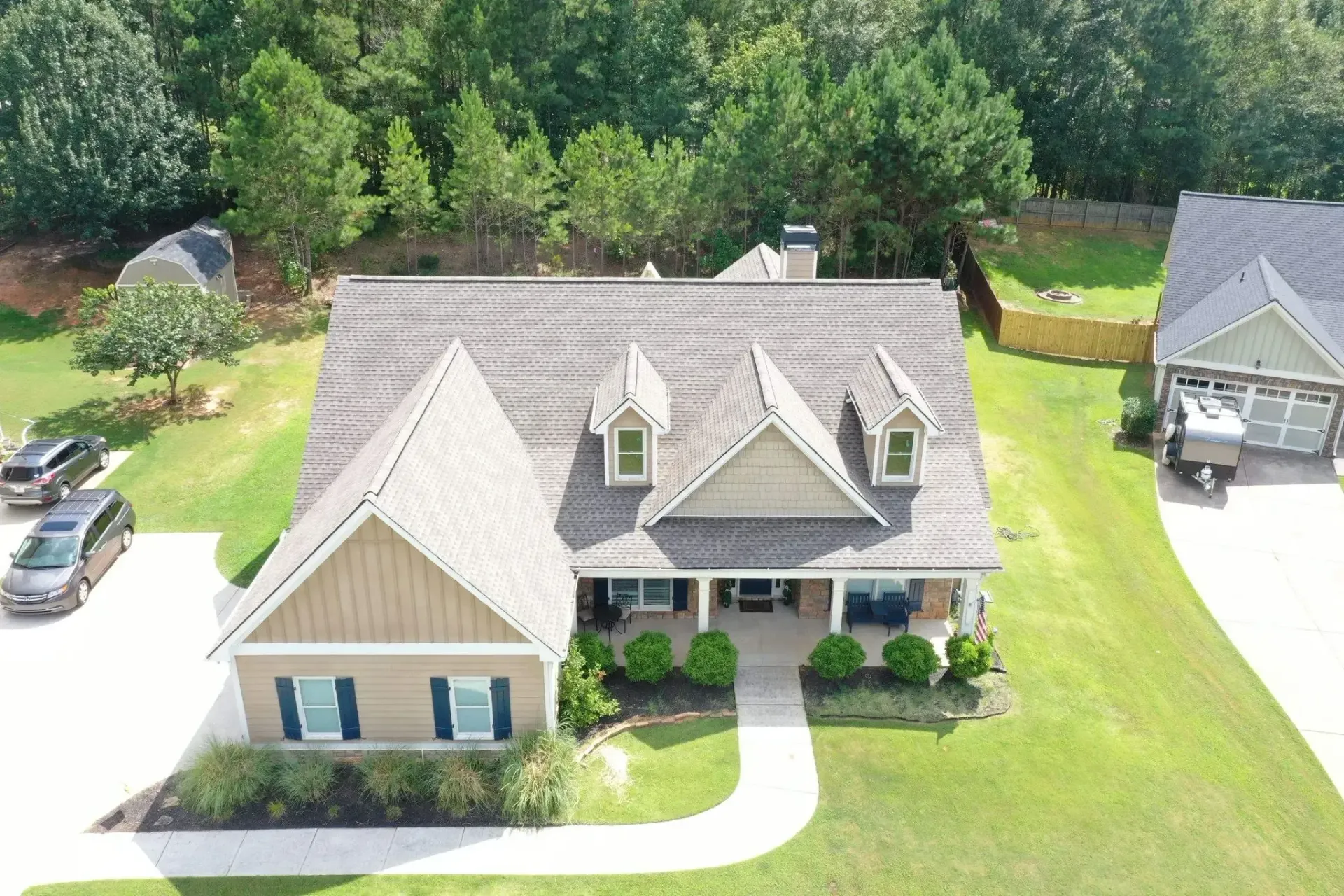House with tan siding, blue shutters, and a long front porch. Green lawn and trees surround the home.