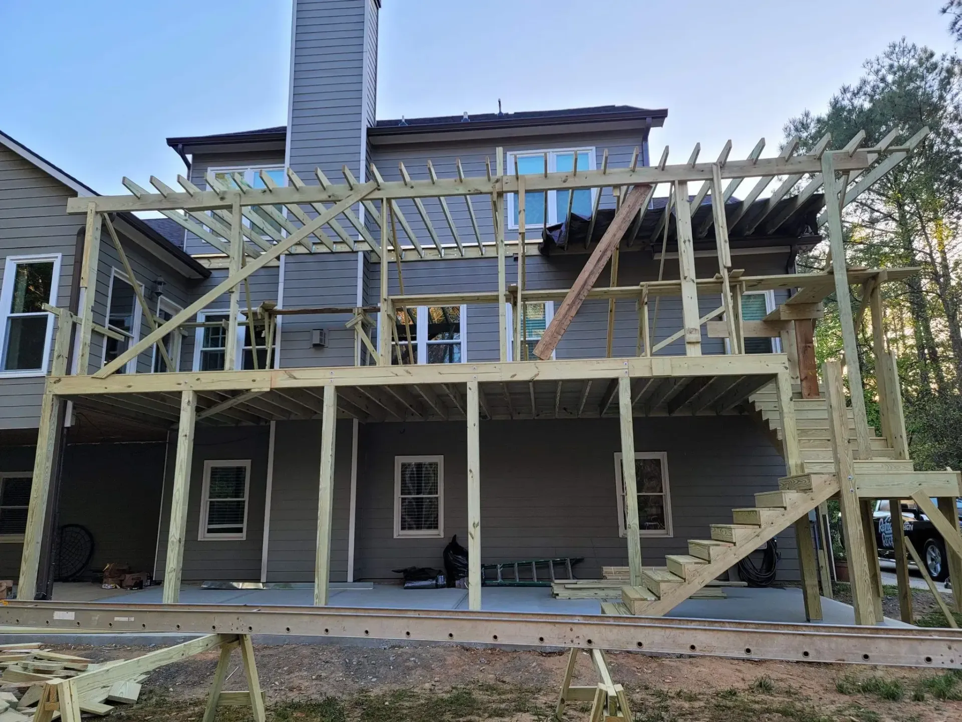 Wooden deck under construction attached to a gray house, with pergola framing and stairs.