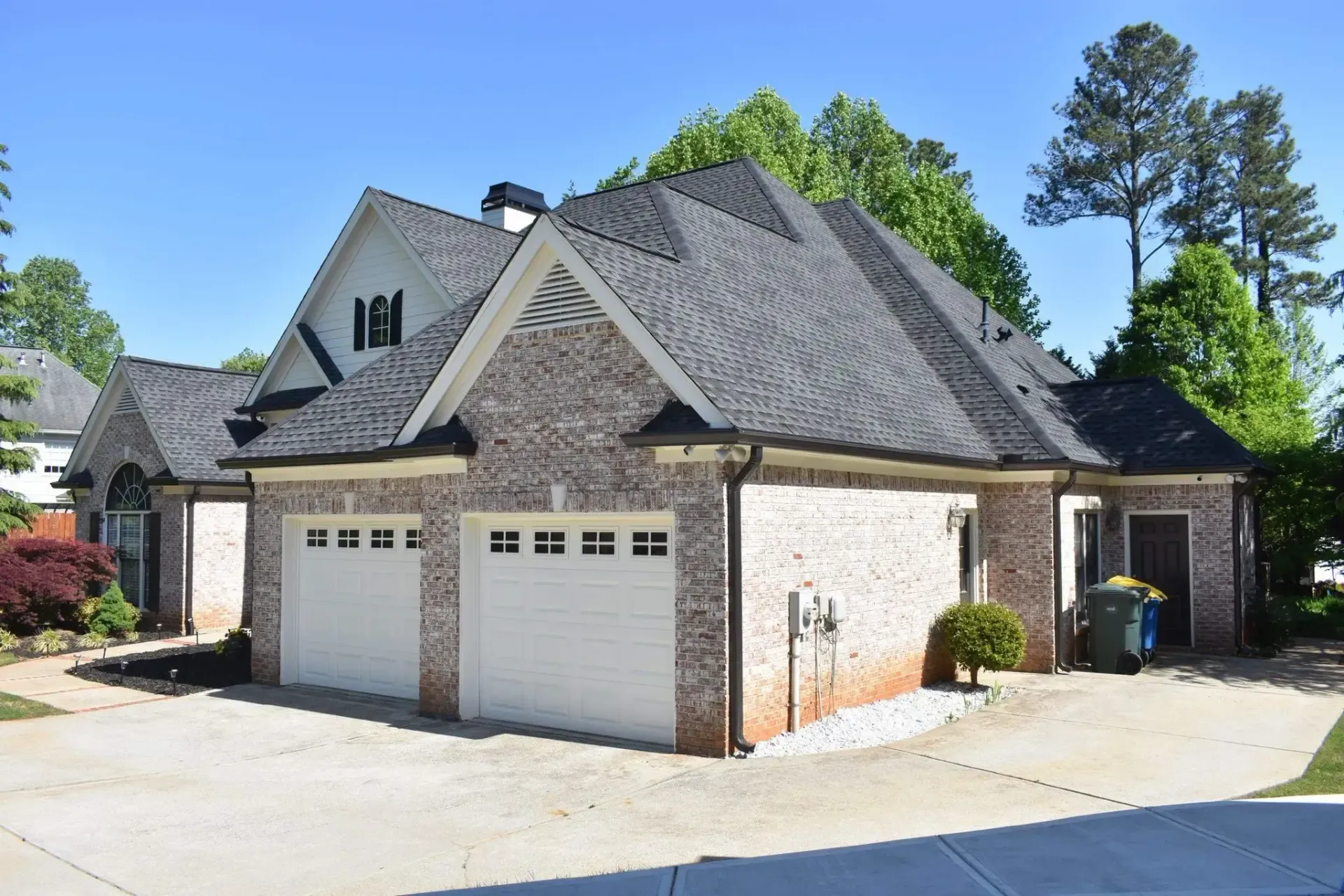 House with gray roof, brick siding, two-car garage, and driveway on a sunny day.