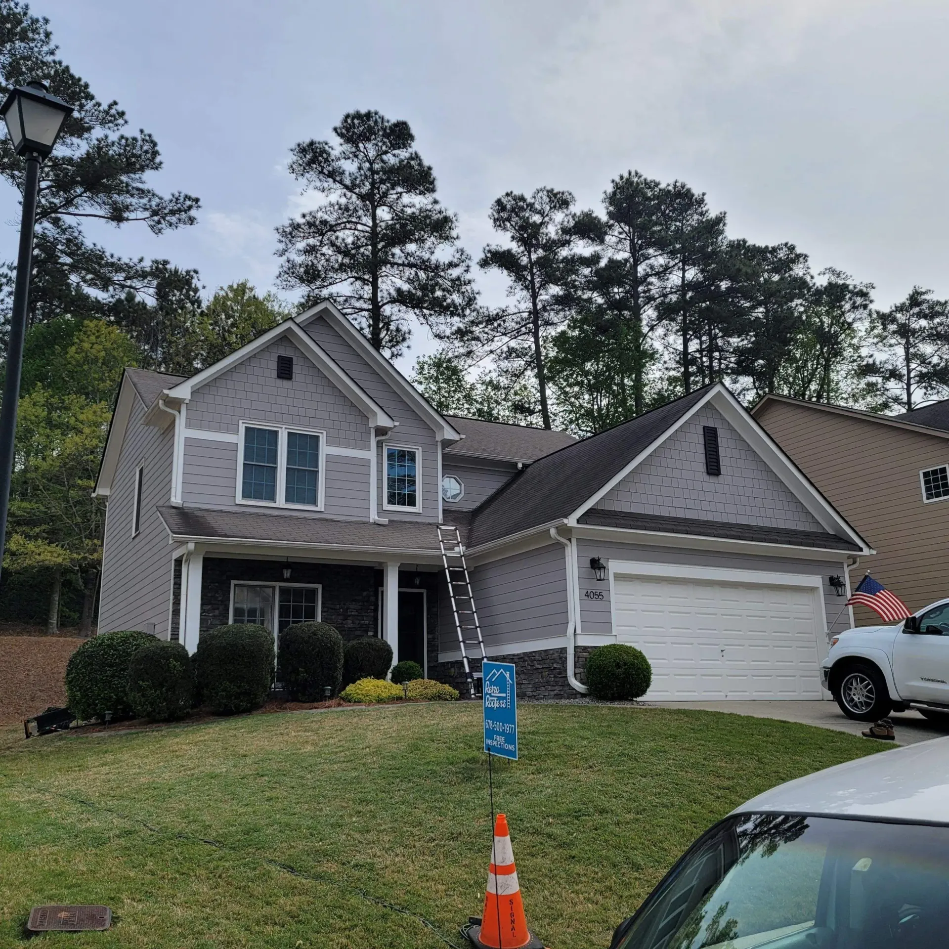 Two-story house with gray siding, a white garage door, and a ladder propped against the roof.