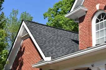 Red brick house with dark roof, white trim, and a clear blue sky.