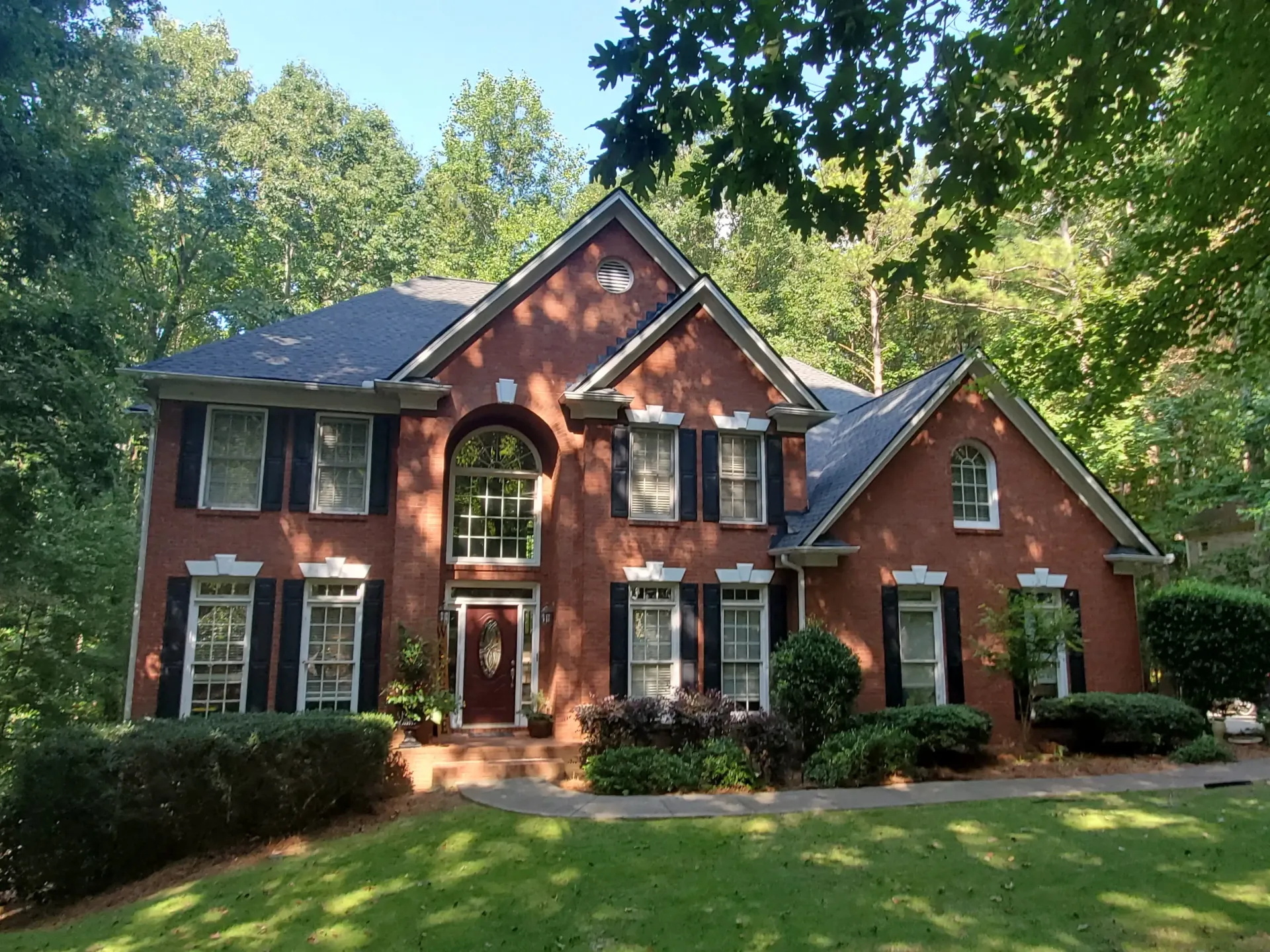 Two-story brick house with black shutters, arched front window, and manicured landscaping.