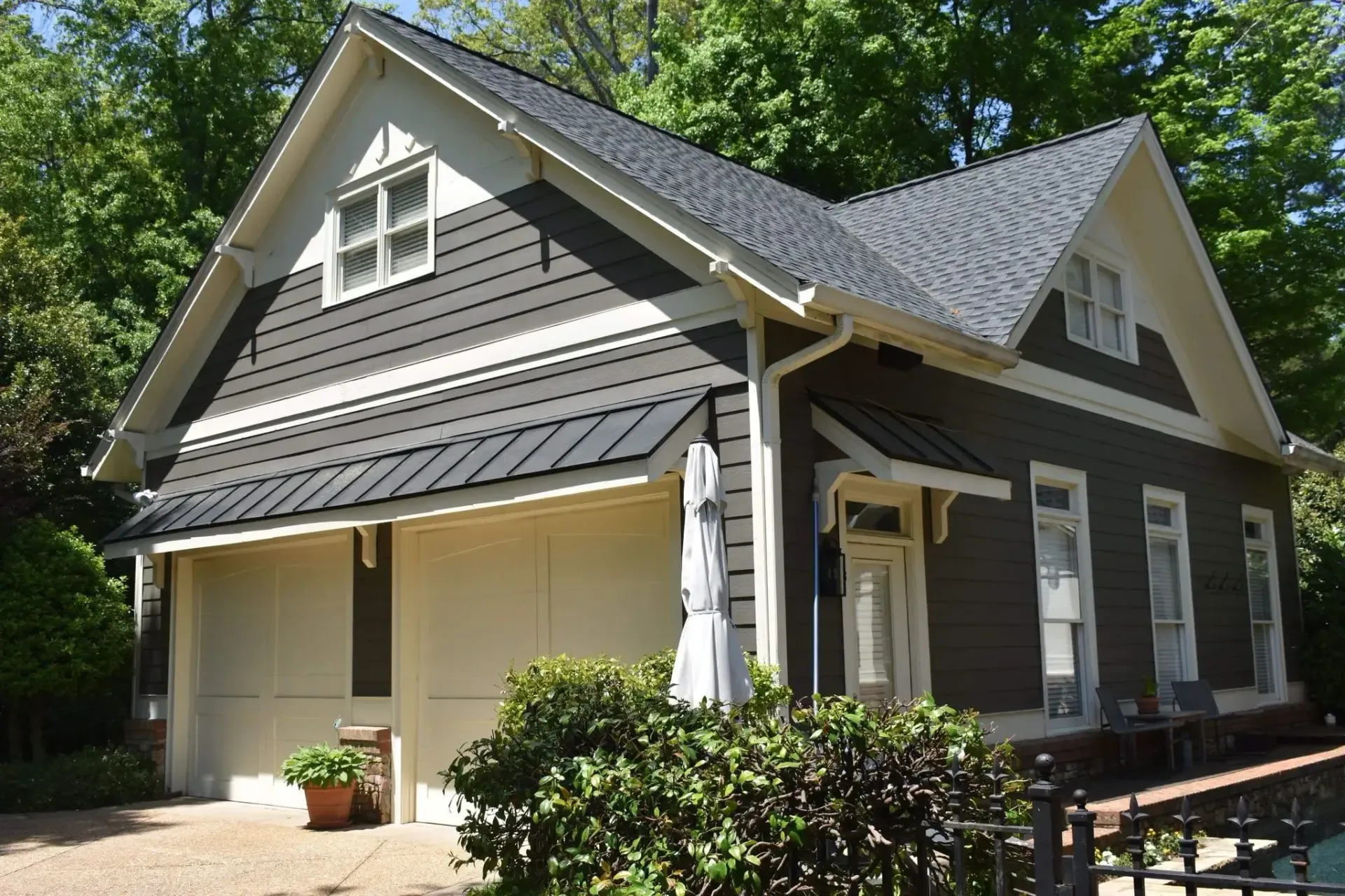 Tan and brown two-story house with a garage, surrounded by trees and a small fence.