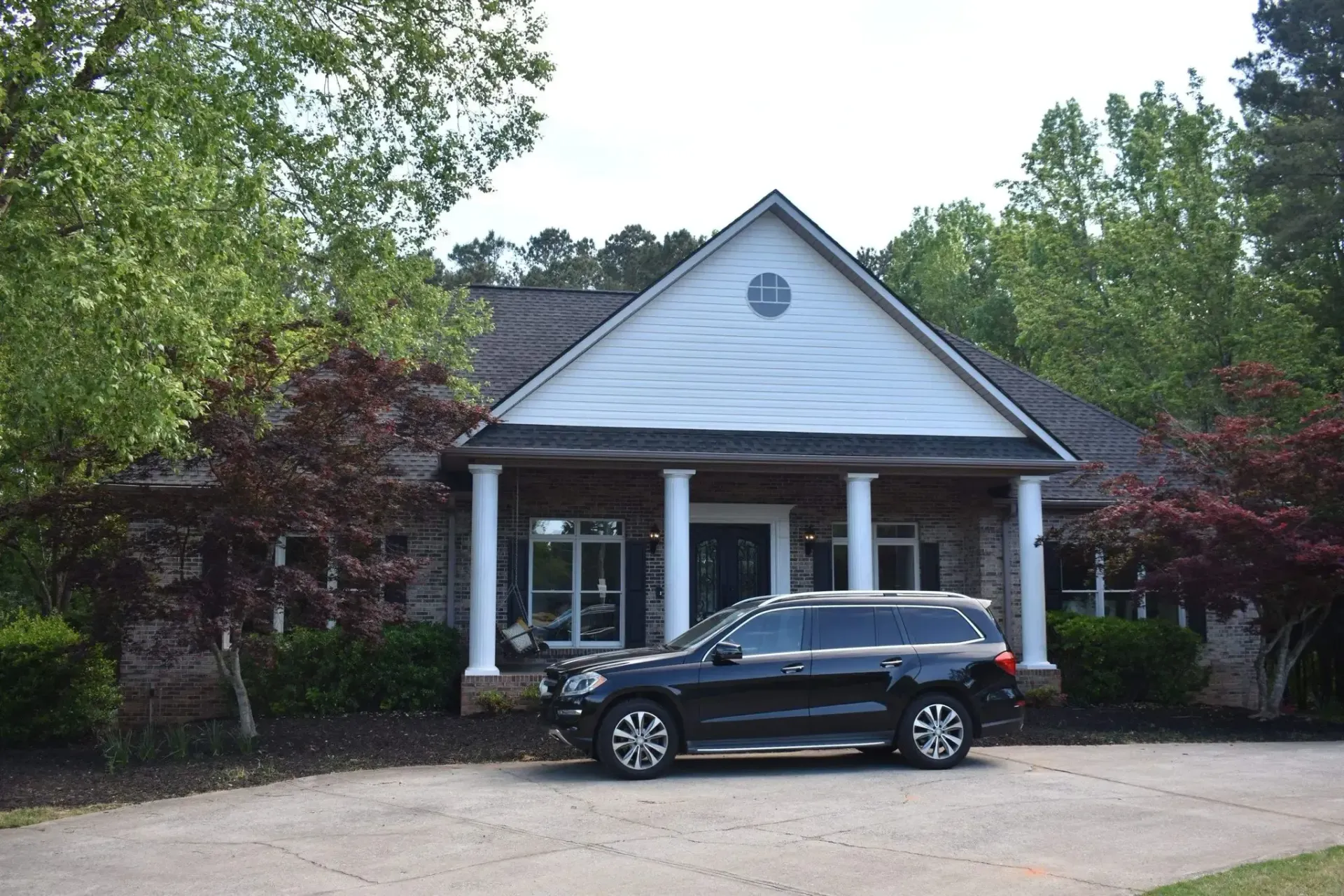 Black SUV parked in front of a building with columns and a brown roof, surrounded by trees.