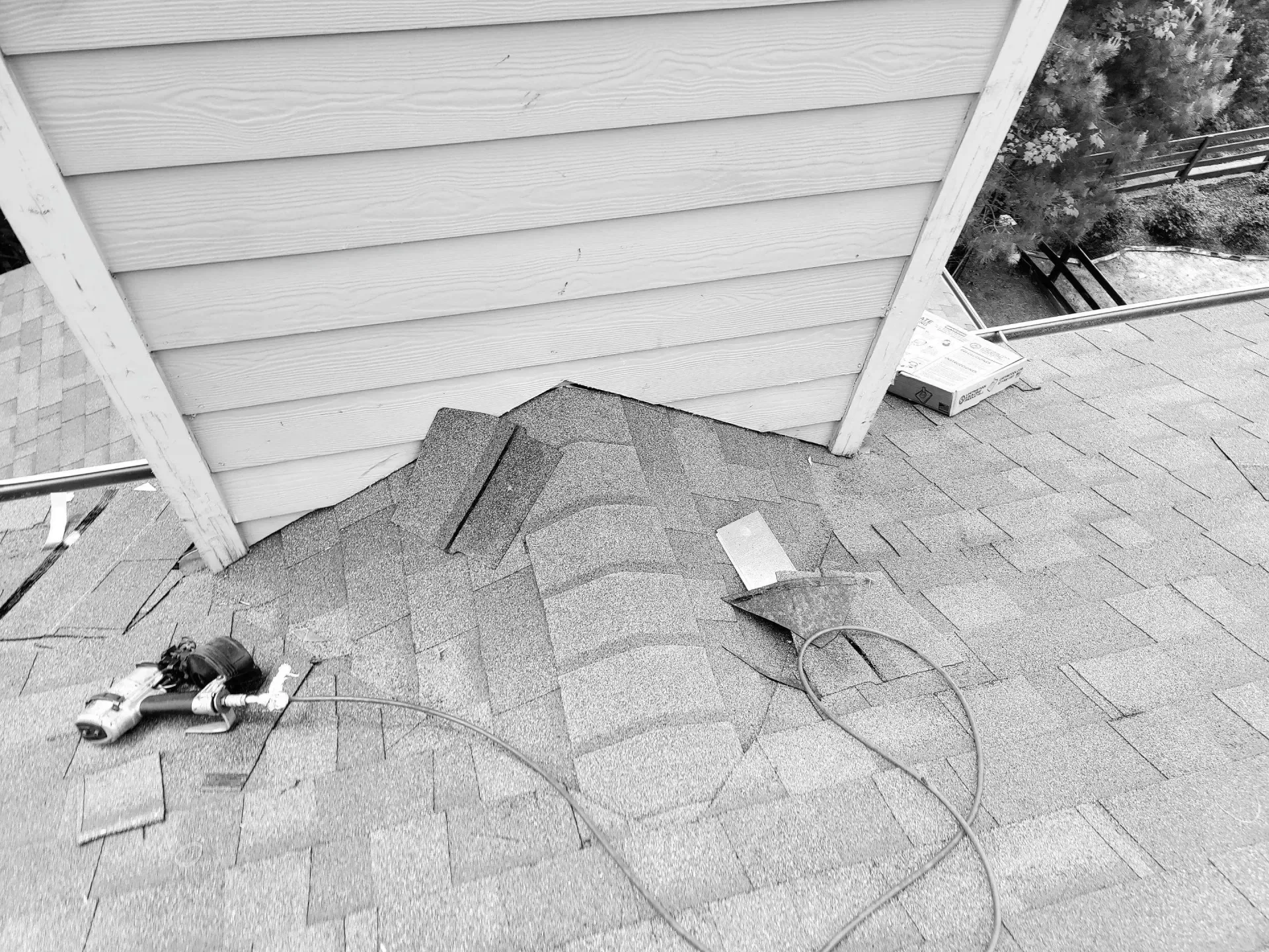 Roof shingles being repaired near a wall's siding; nail gun and tools on the roof.
