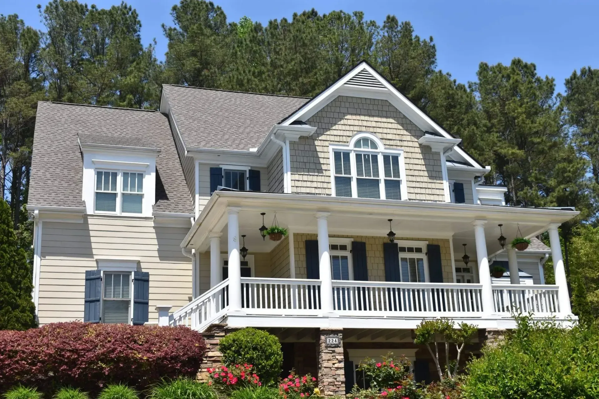 Two-story house with a porch, light siding, blue shutters, and a gray roof, set against trees.