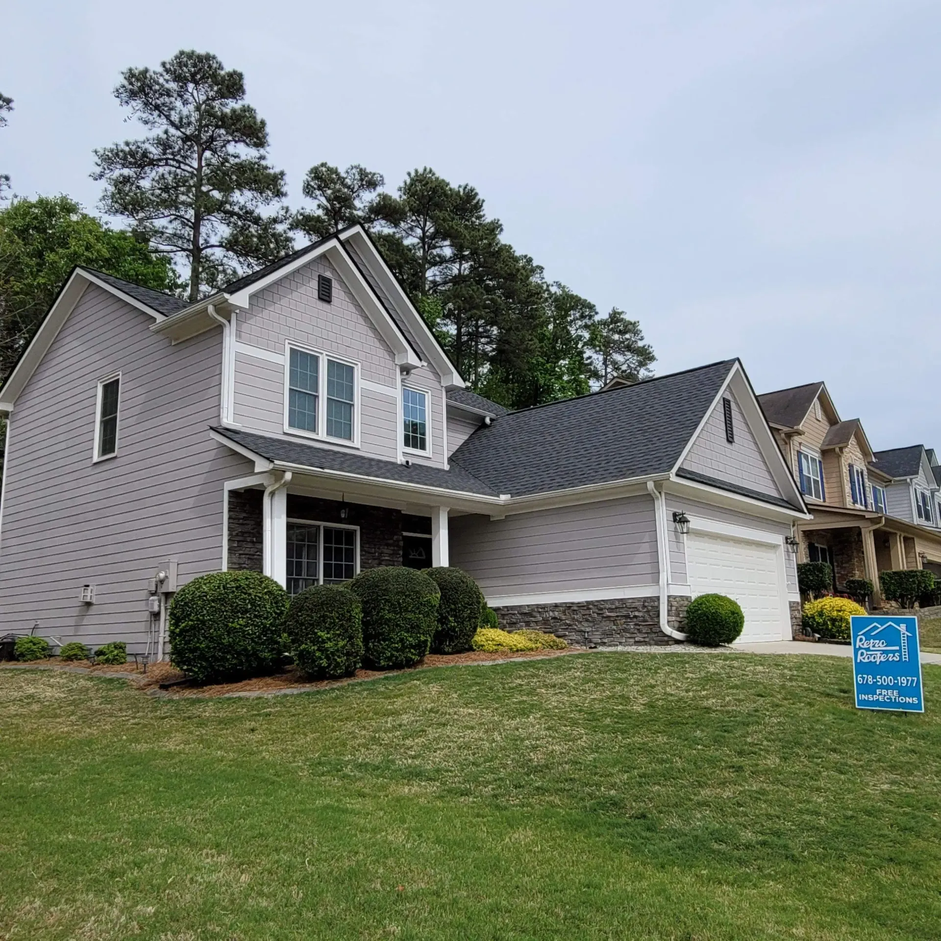 Gray house with new dark roof and garage, green lawn, sign in yard.