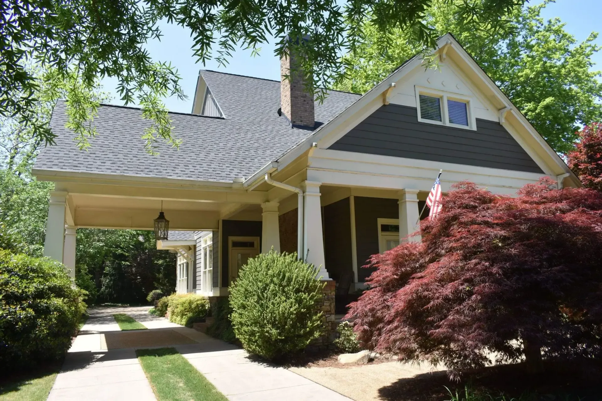 Curb-appeal view of a house. White trim, dark green siding, covered carport, and a red Japanese maple tree.