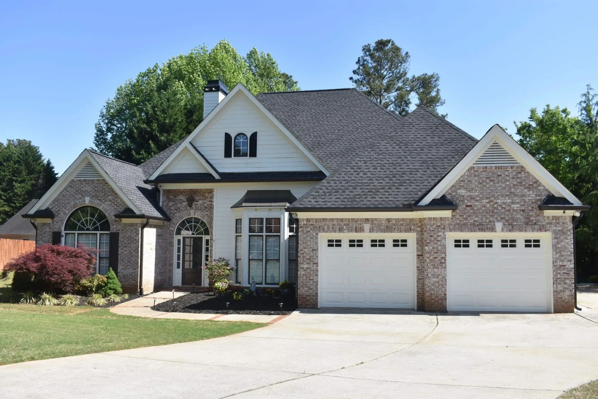 Suburban house with gray roof, brick and white siding, and two-car garage under a blue sky.