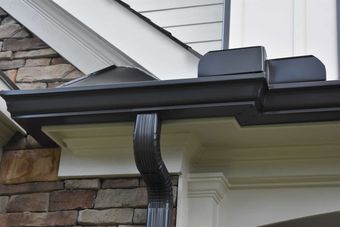 Black rain gutter attached to a house with white trim and stone exterior.