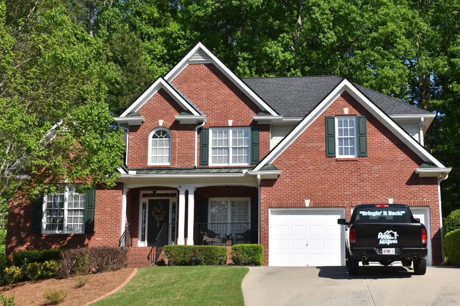 Brick house with green shutters, white garage door, and black truck parked in the driveway.