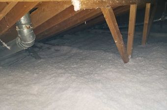 Attic interior with white insulation, wooden beams, and a silver duct.