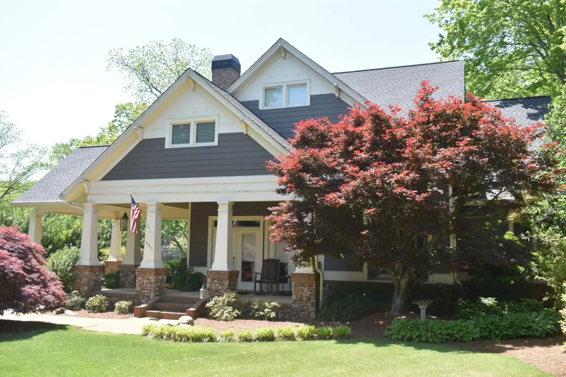 Craftsman-style home with a porch, brown siding, white trim, and a red tree in the front yard.