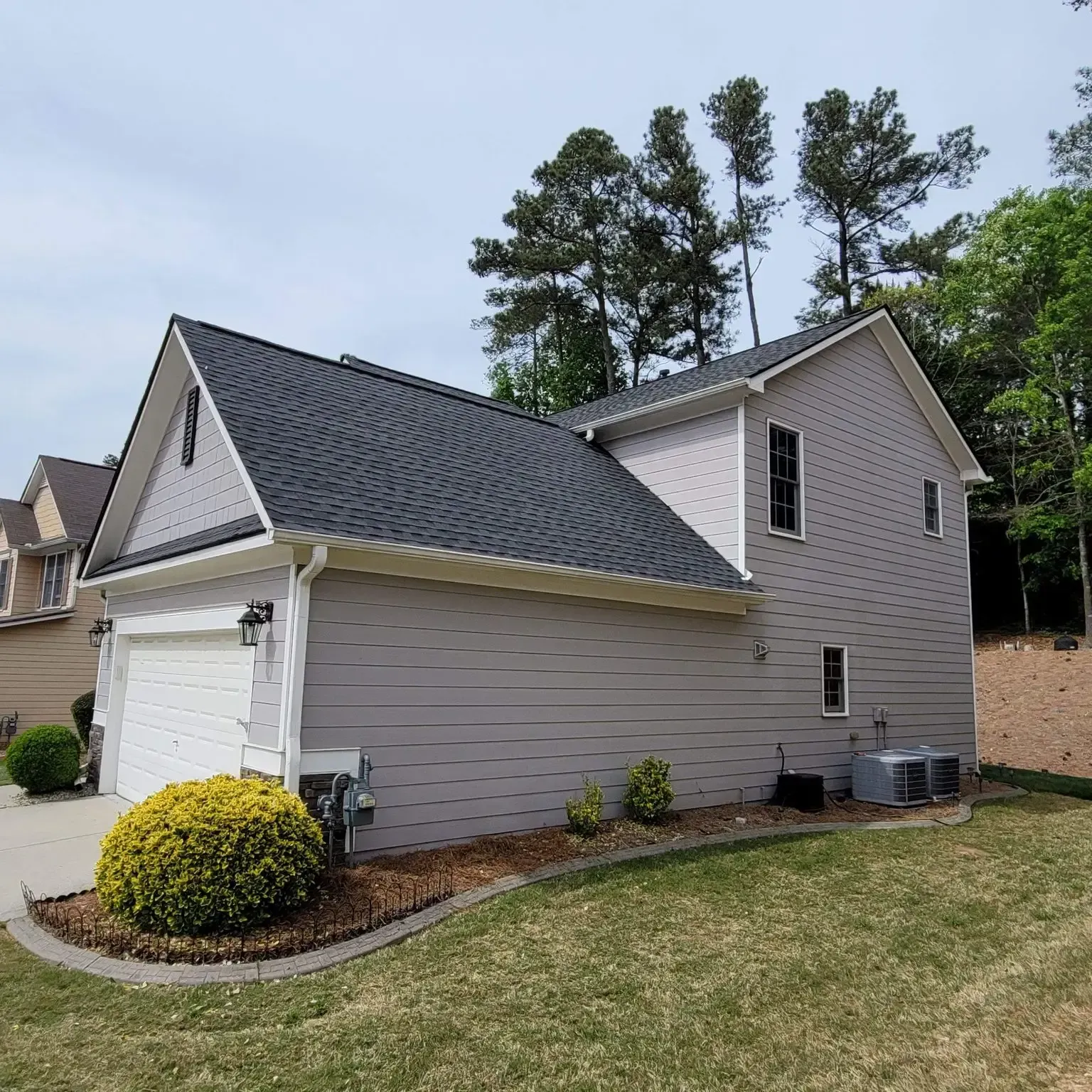 Gray two-story house with a black roof, white garage door, and green lawn.