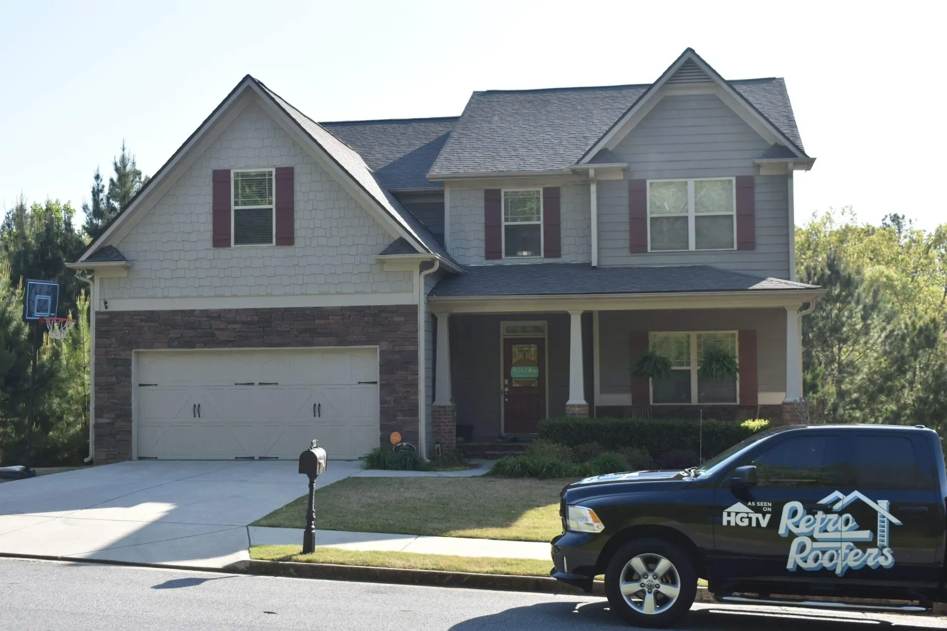 Two-story house with gray siding, brick facade, and a black HGTV truck parked in the driveway.