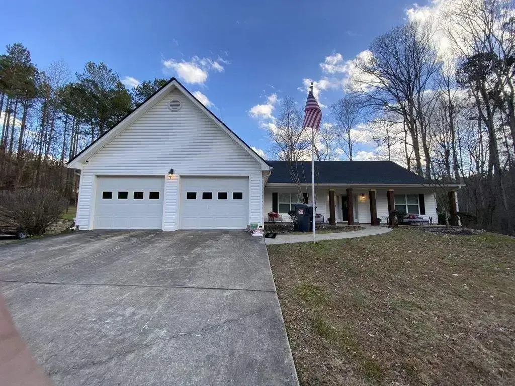 White house with a two-car garage, a flag, and a concrete driveway on a sunny day.