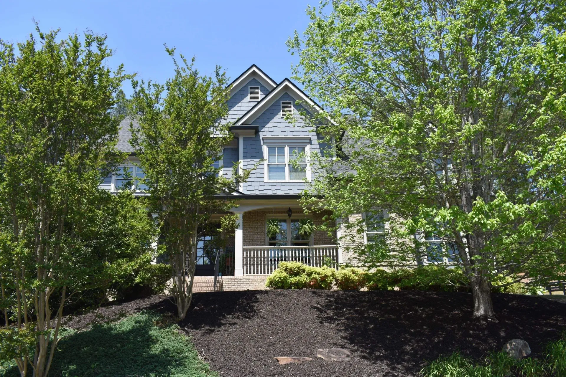 Two-story house with blue siding, a porch, and trees. Black mulch in the yard.