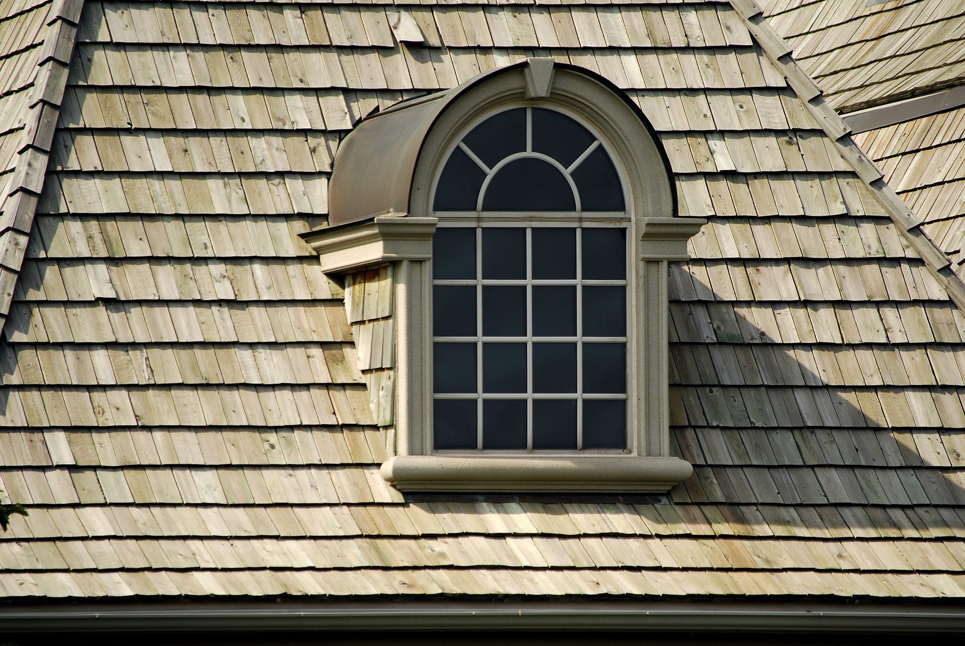 Dormer window with arched top on a cedar shake roof.