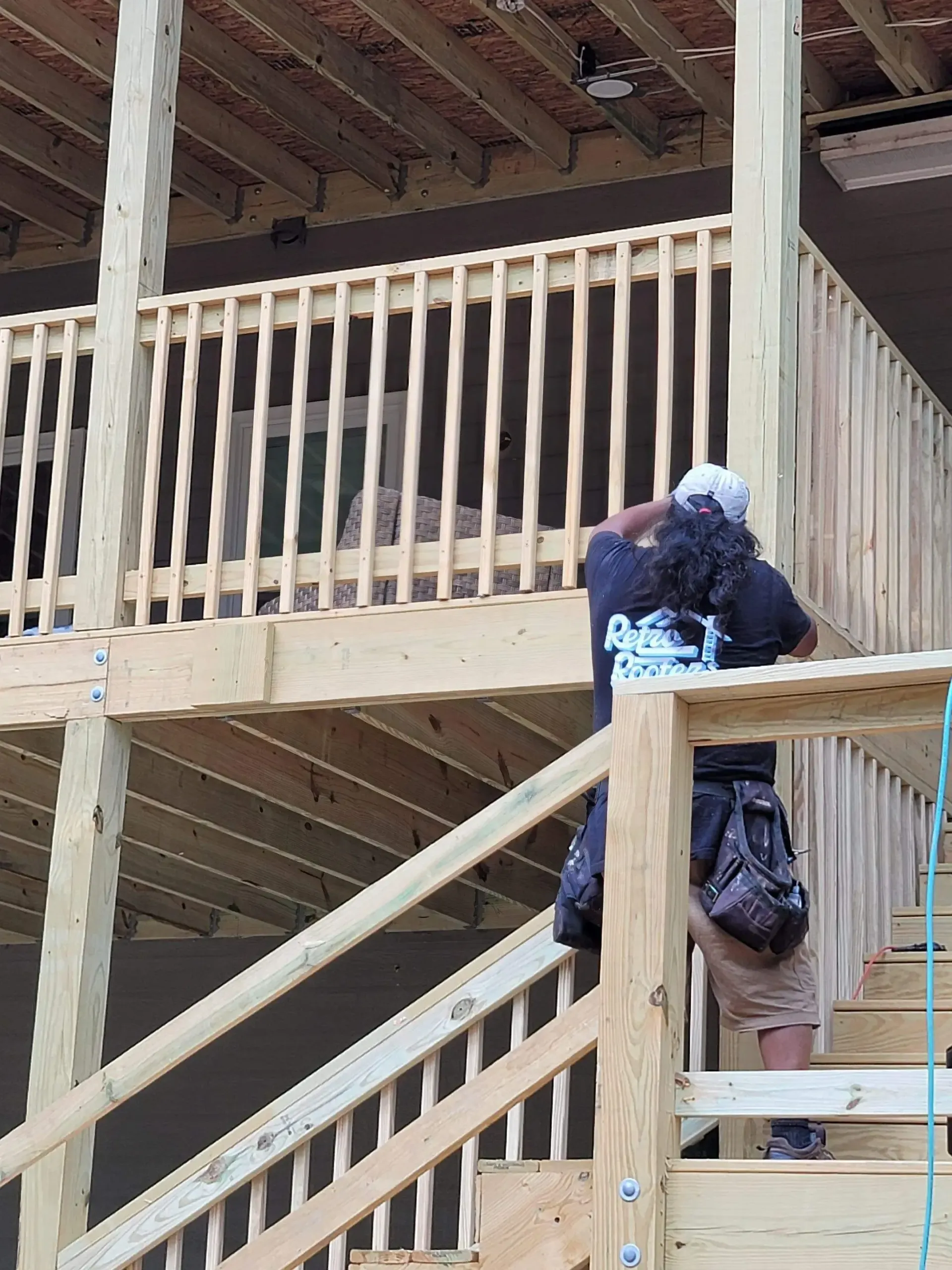 Person on wooden staircase, looking up. New deck under construction with railing.