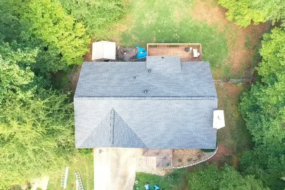 Overhead view of a house with a gray roof, surrounded by green trees and a grassy yard.