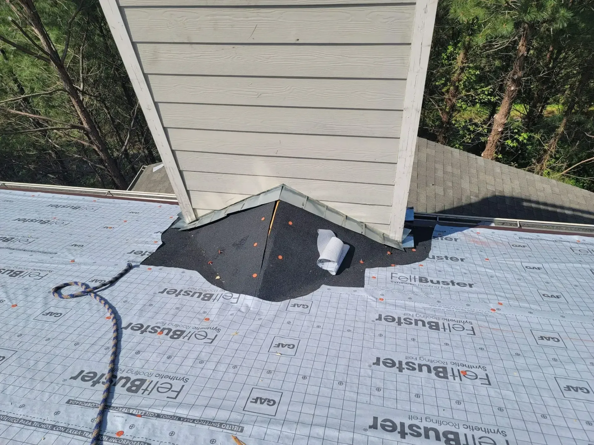 Chimney on a roof, black flashing, surrounded by gray underlayment.