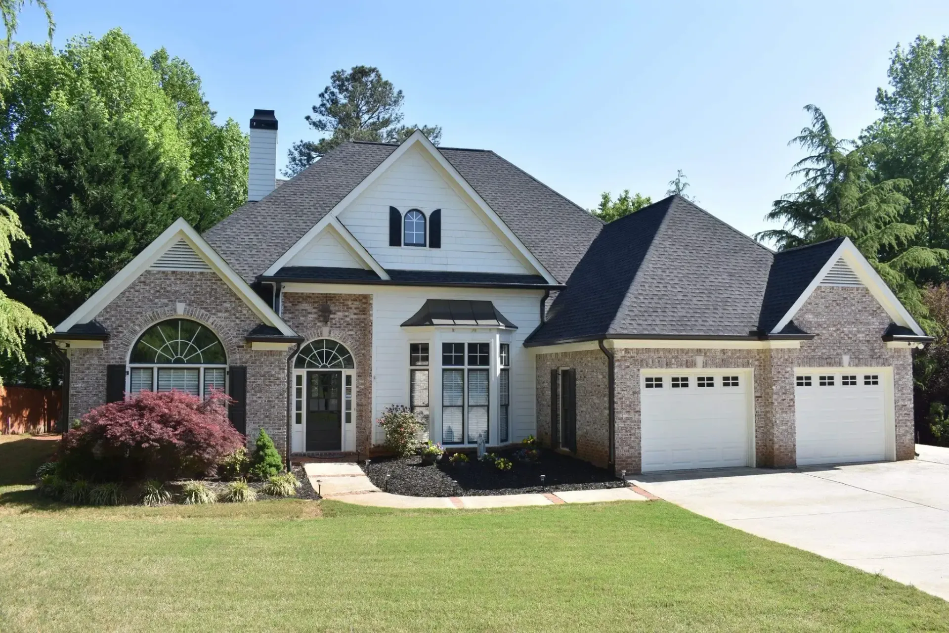 Two-story house with brick accents, white stucco, and a three-car garage, set on a green lawn.