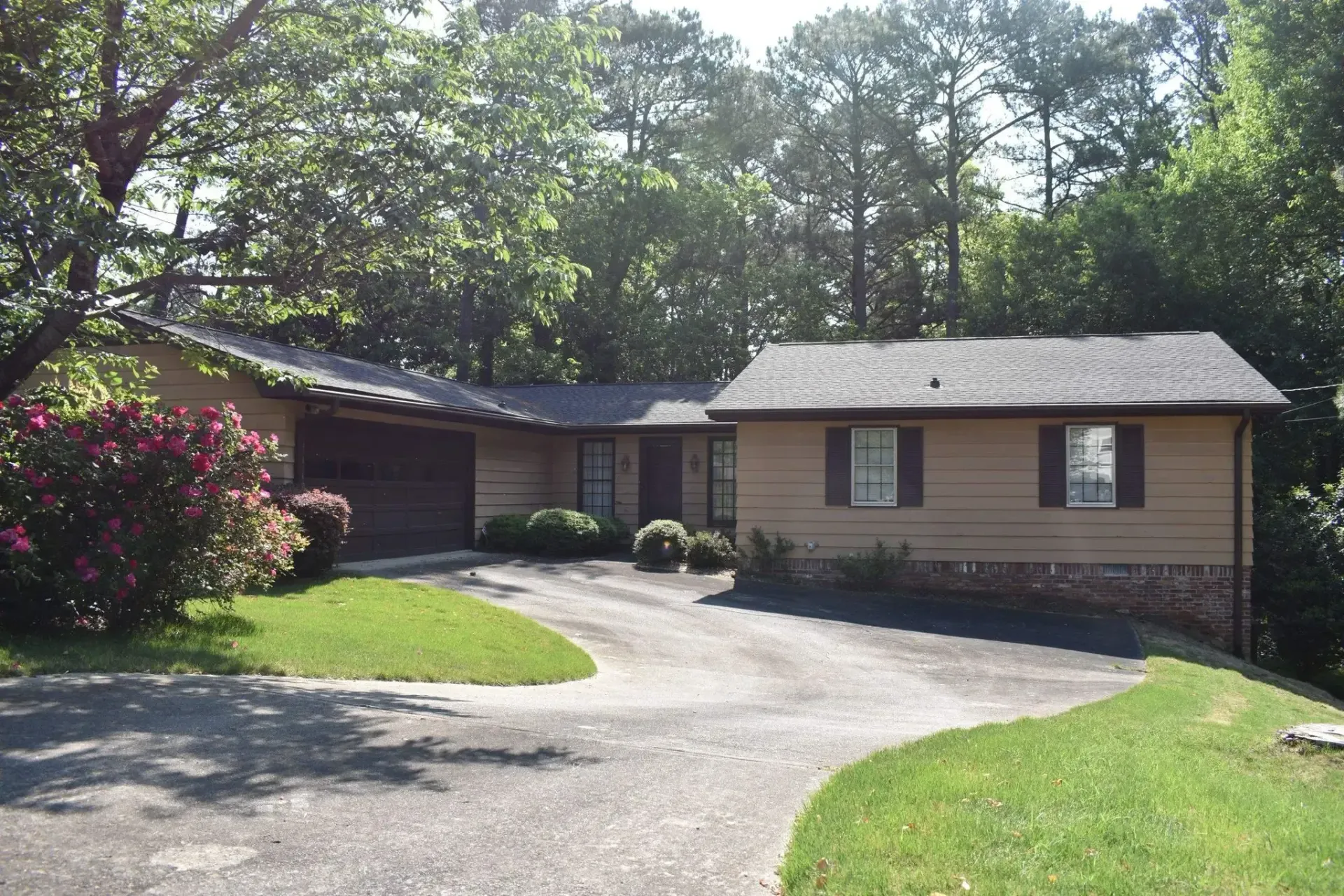 Tan and brown house with driveway, grass, and trees.