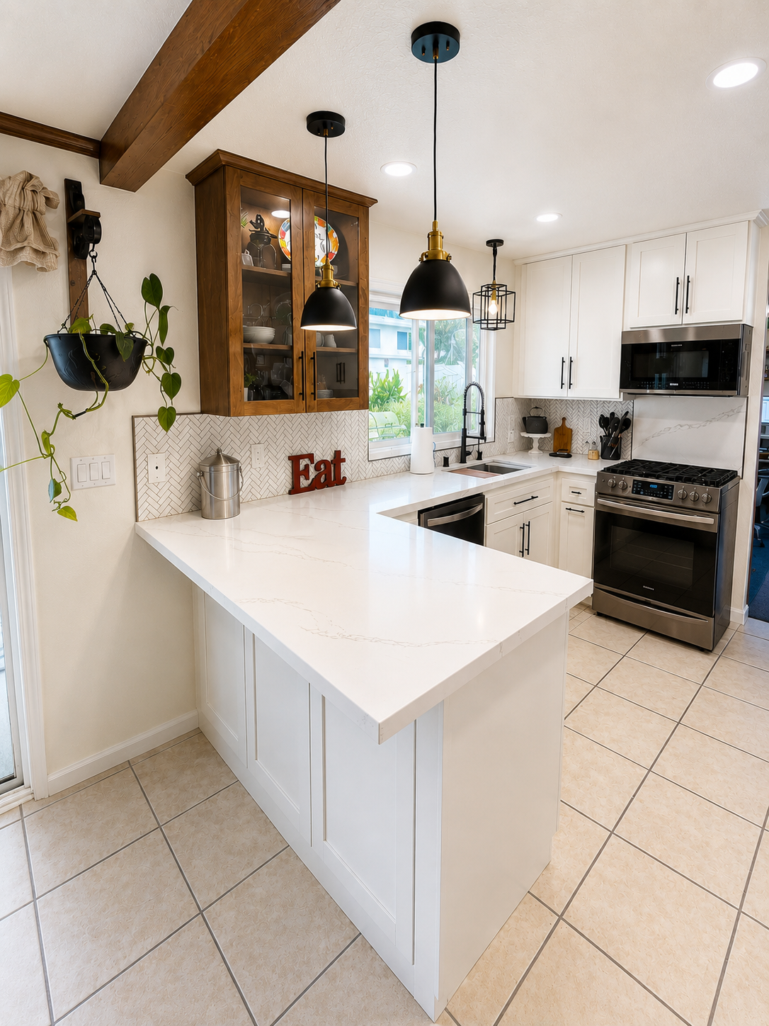 Bright white kitchen with island, black pendant lights, wood accents, and stainless-steel stove and microwave.