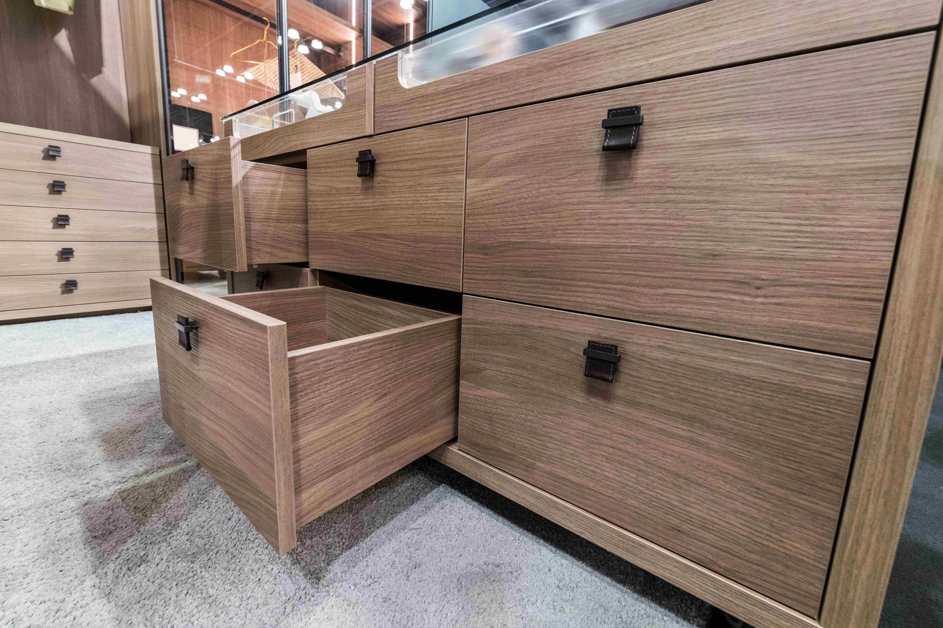 Wooden dresser with one drawer open in a store showroom, showing a modern wood grain finish.