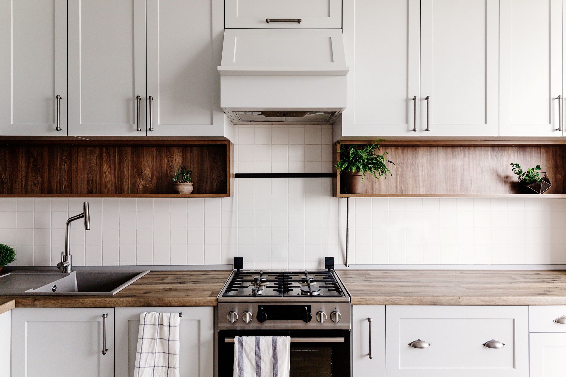 Modern white kitchen with wooden countertops, stove, sink, cabinets, and small plants