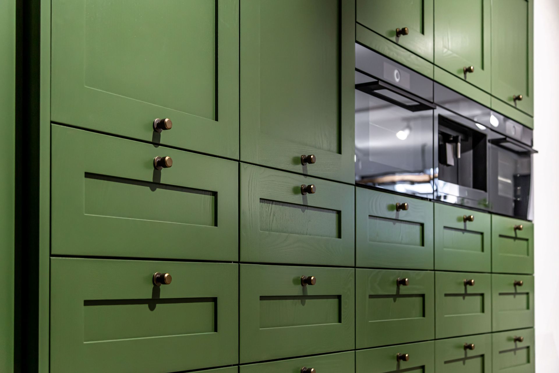 Green kitchen cabinets with black handles and built-in appliances