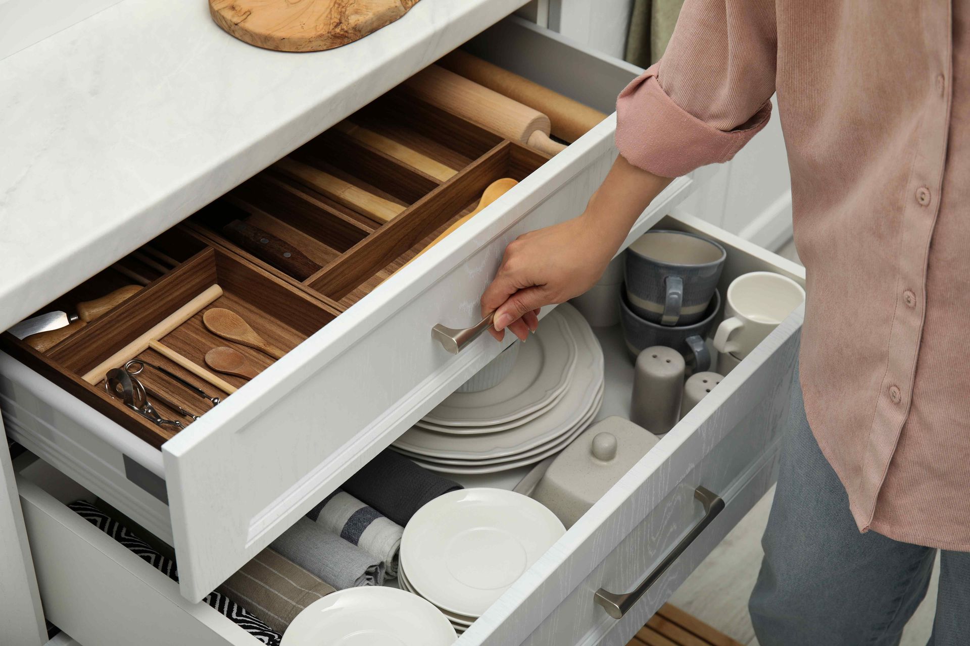 Person opens a kitchen drawer with organized utensils, plates, and a coffee maker nearby.