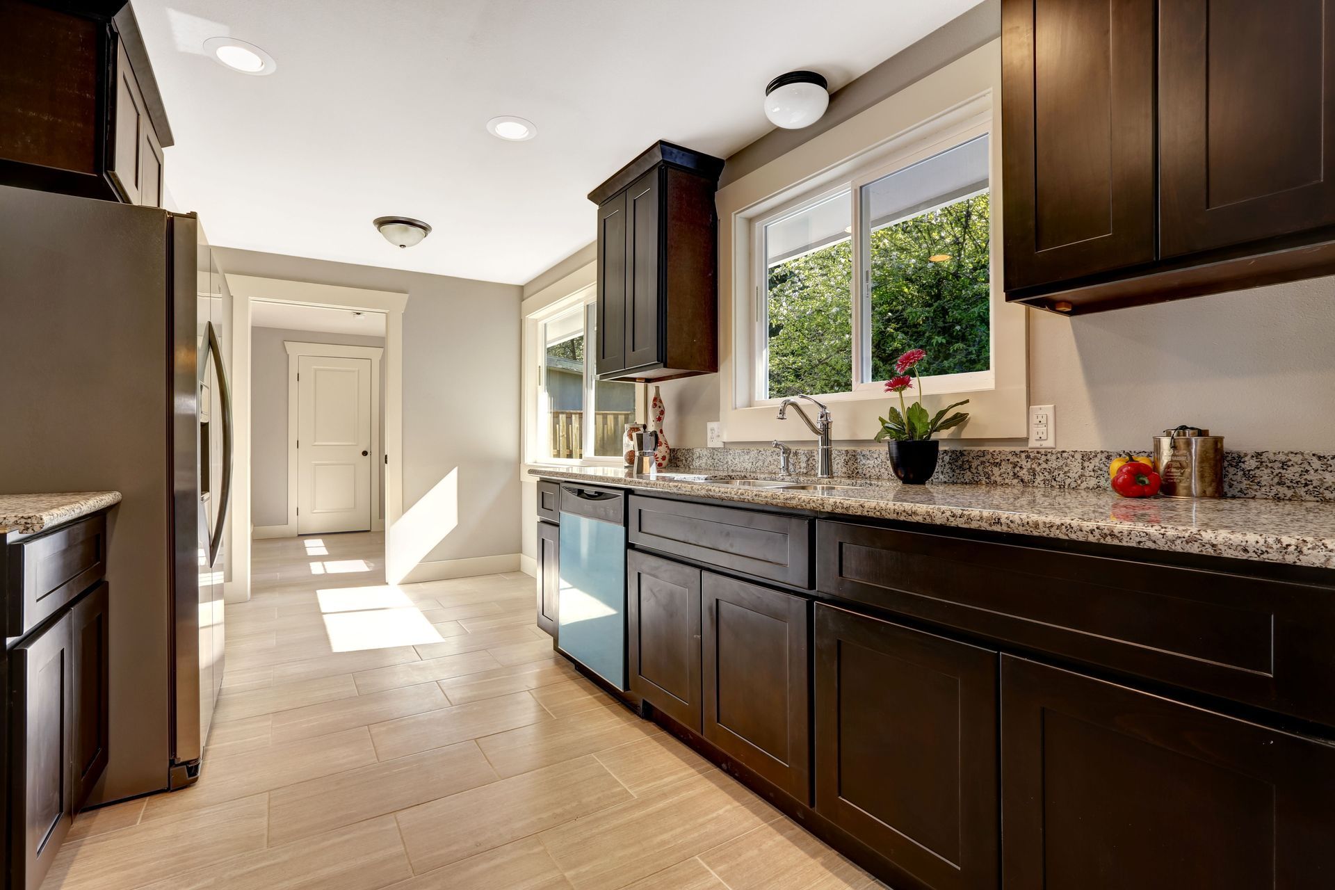 Bright kitchen with dark cabinets, stainless appliances, white countertops, and sunlight from a large window.