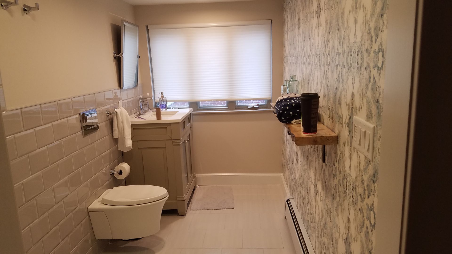 Small bathroom with a toilet, sink, window blinds, and patterned wallpaper.