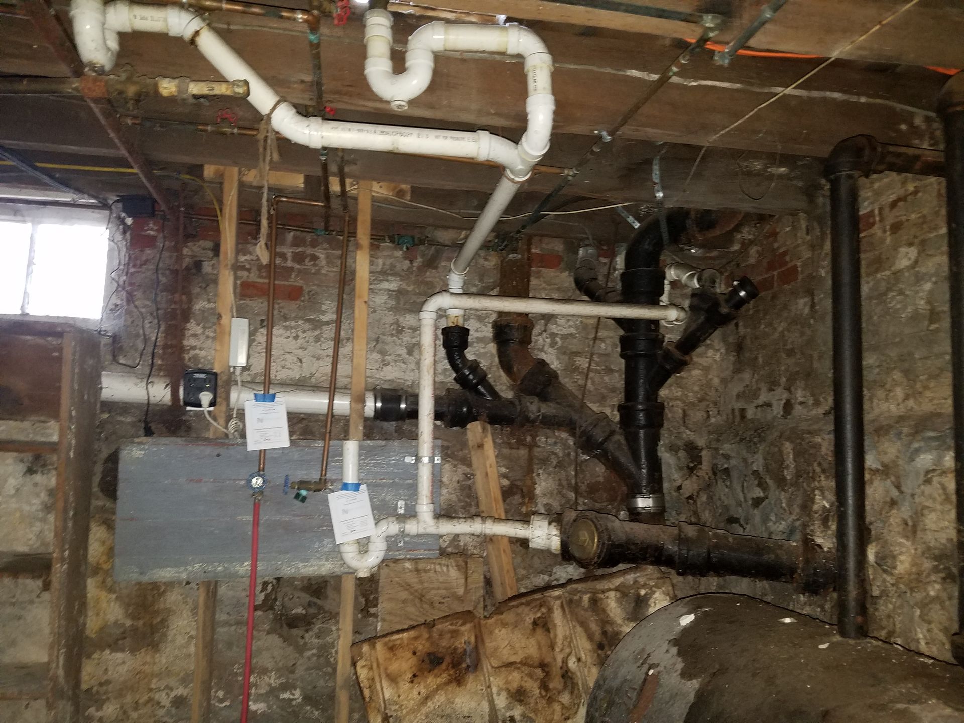 Exposed basement utility room with pipes, ductwork, and stone walls around a boiler or furnace