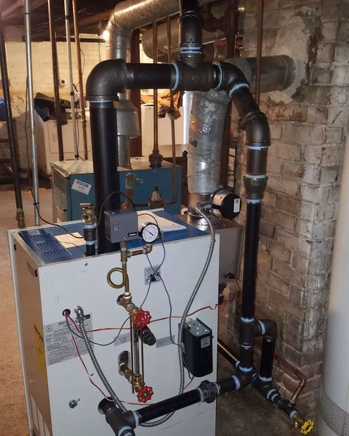 Basement boiler and heating system with black insulated pipes, gauges, and control panel against a brick wall