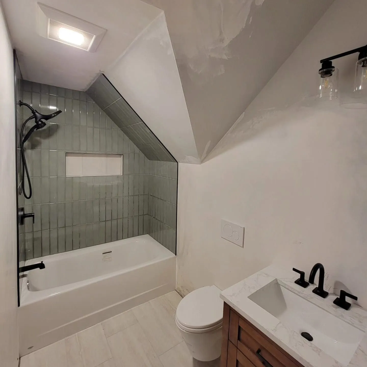 Small white bathroom with a tiled shower-tub, toilet, and sink beneath a sloped ceiling.