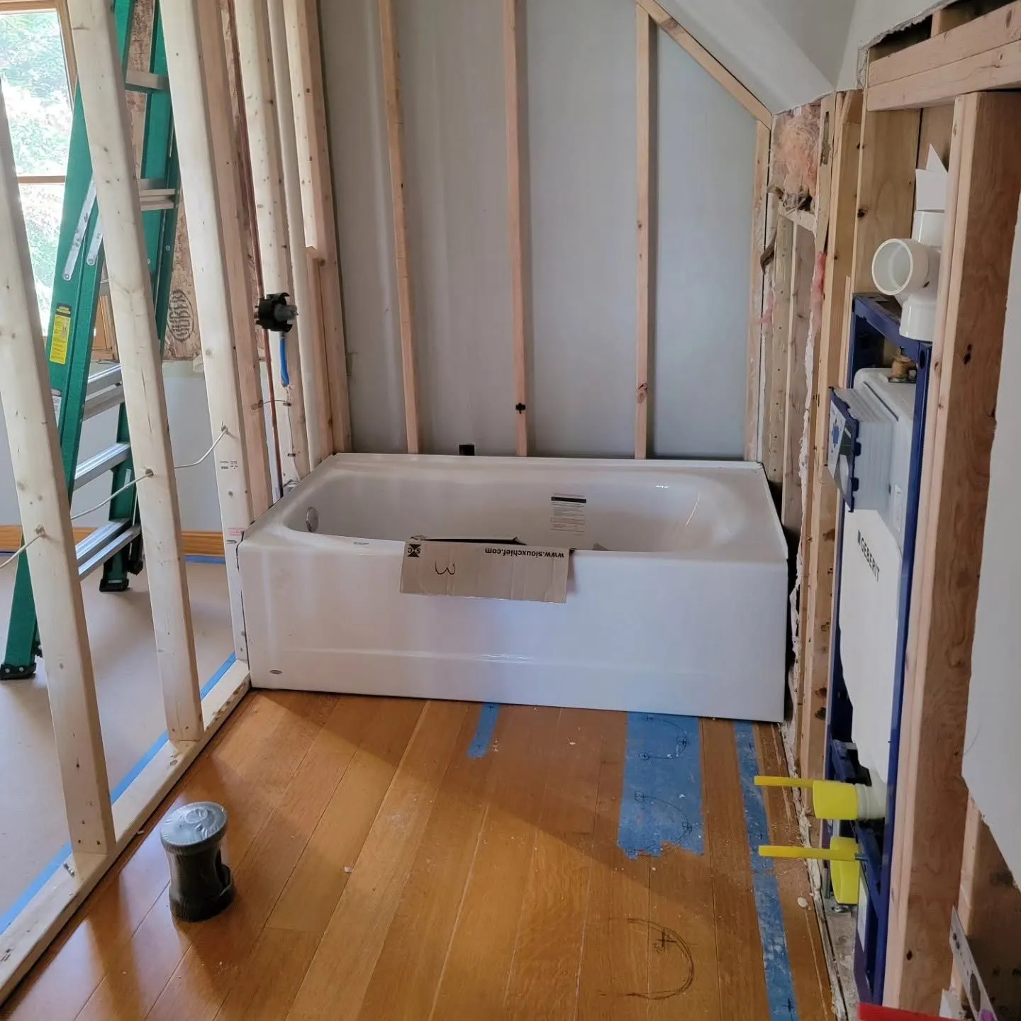 Bathtub installed in unfinished bathroom with exposed wall framing and wood subfloor