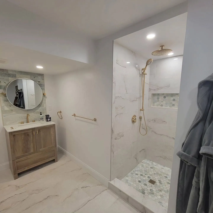 Modern white bathroom with marble shower, wooden vanity, and round mirror