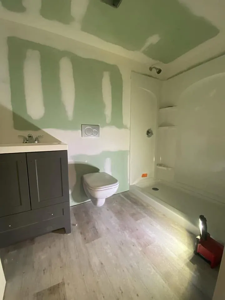 Partially renovated bathroom with green drywall patches, vanity, toilet, and tub under construction