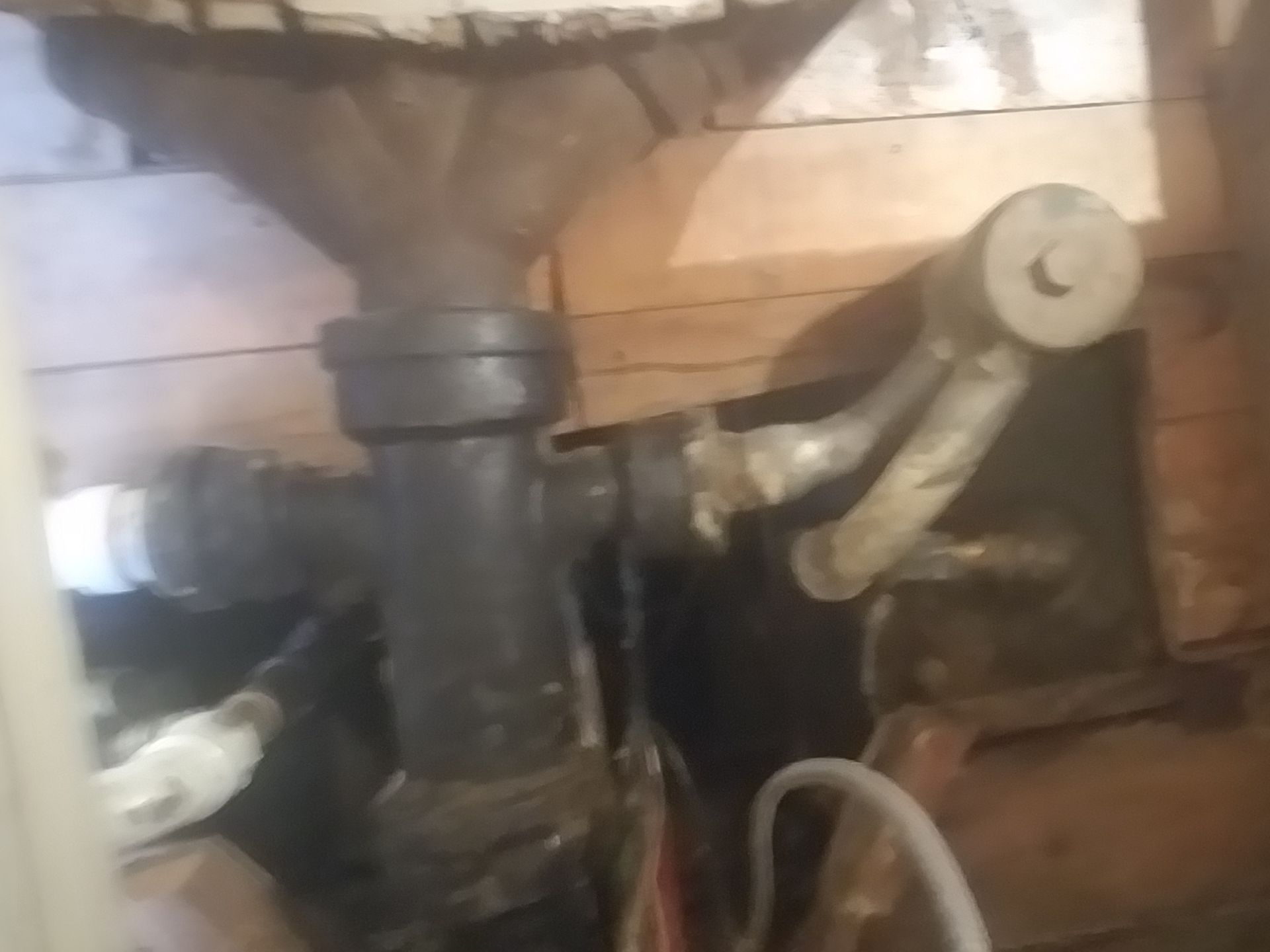 Close-up of a black pipe with a valve and a metal lever against a wooden wall.