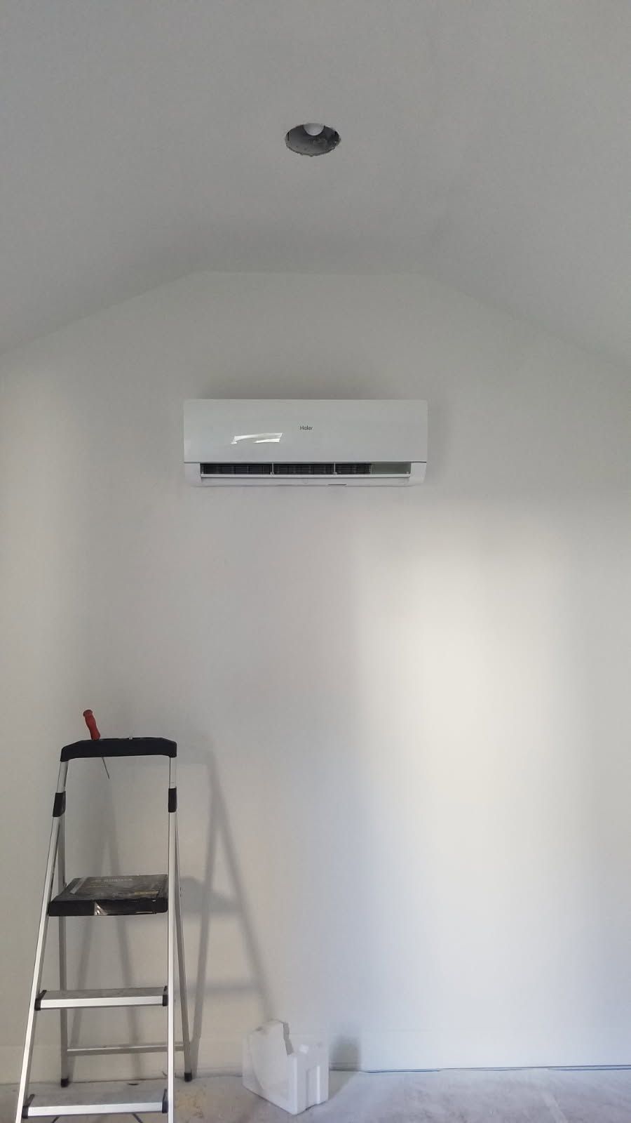 Small room with a wall-mounted air conditioner, ladder, and paint supplies under a curved white ceiling.